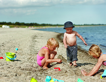 Tre børn leger i sandet ved vandkanten på stranden