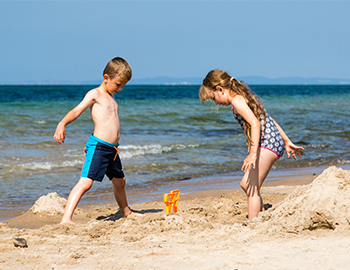 To børn leger i sandet på stranden med havet i baggrunden