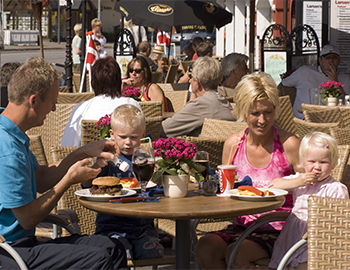To forældre og to børn sidder udenfor ved et bord på en café og spiser